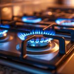 Gas range stovetop with four burners on with blue flames. There is a tile backsplash and speckled granite counter.