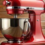 A bold red stand mixer with a gleaming stainless steel mixing bowl sits on a wooden countertop. Behind it, warm-toned wooden paneling enhances the rustic charm of the setting.