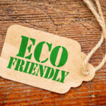 Brown kraft paper tag with scalloped edges and a twine string, featuring the bold green text “ECO FRIENDLY” on a rustic wooden background.