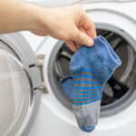Hand holding a single blue striped sock in front of an open washing machine door.