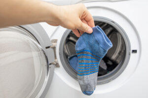 Hand holding a single blue striped sock in front of an open washing machine door.